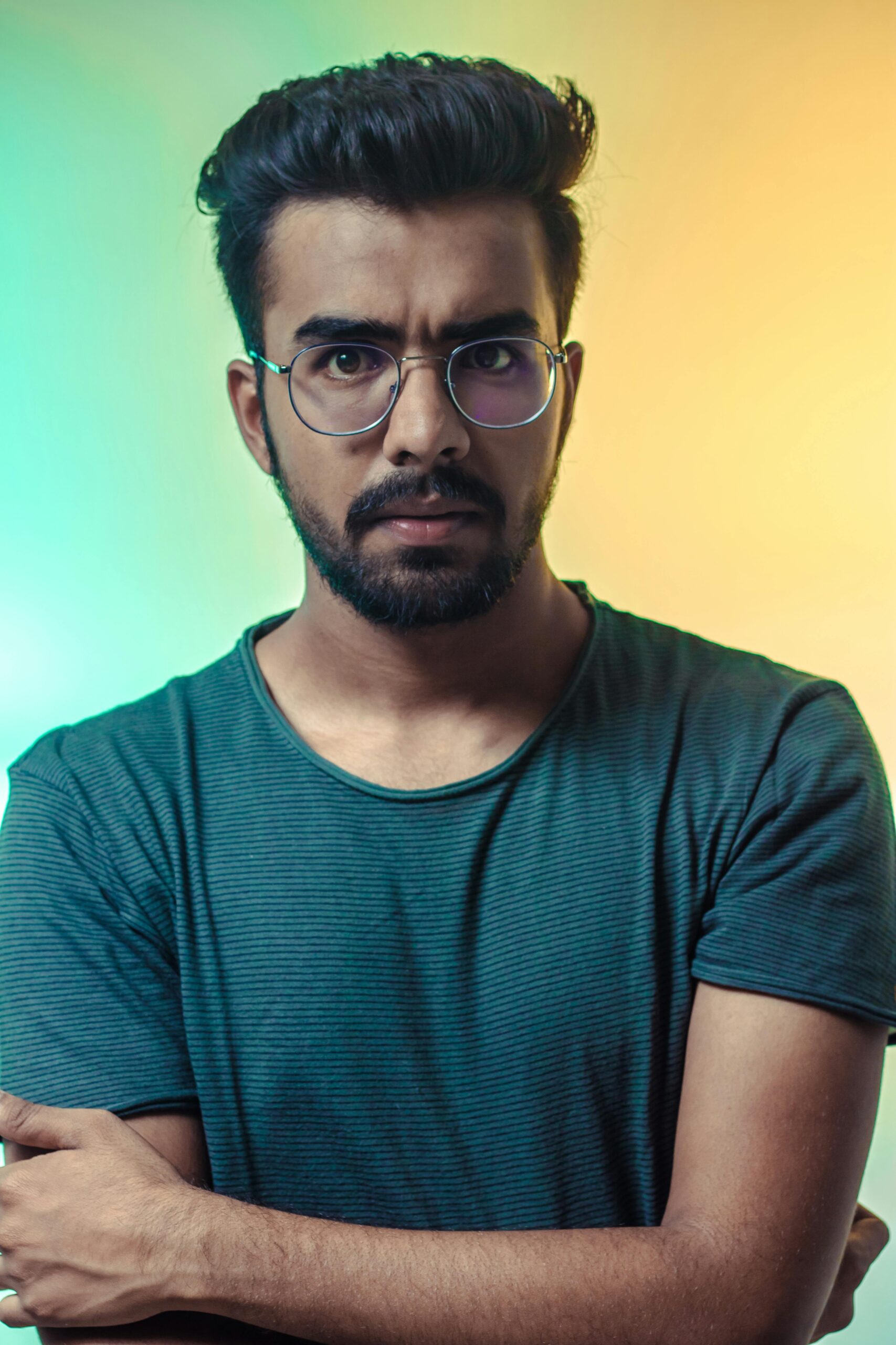 A thoughtful adult man with eyeglasses posing for a portrait with a vibrant backdrop.